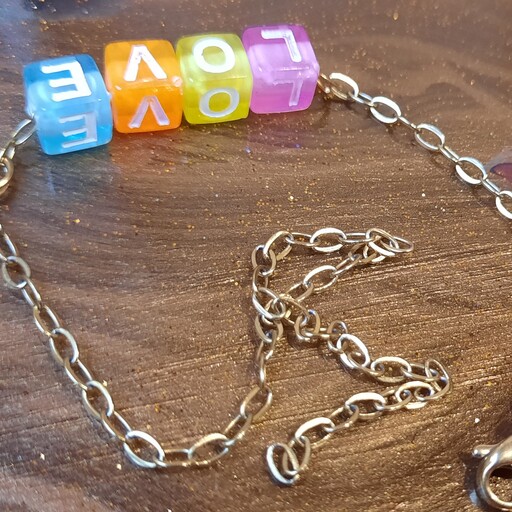 دستبند  لاو با مهره های حروف انگلیسی و زنجیر طلایی رنگ ثابت و ضدحساسیت و قفل طوطی ساخته شده