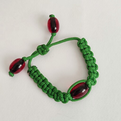دستبند  مکرومه سبز. بافت درشت و برجسته ، بافته شده با مهره قرمز درشت و شفاف و قفل کشویی