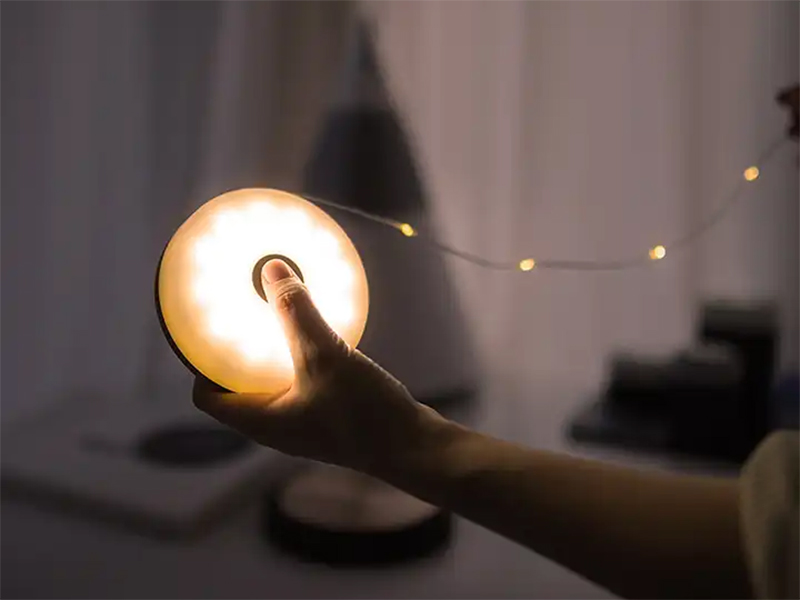 Hand holding a round, bright camping lantern with a string of fairy lights extending from it, for outdoor ambiance.