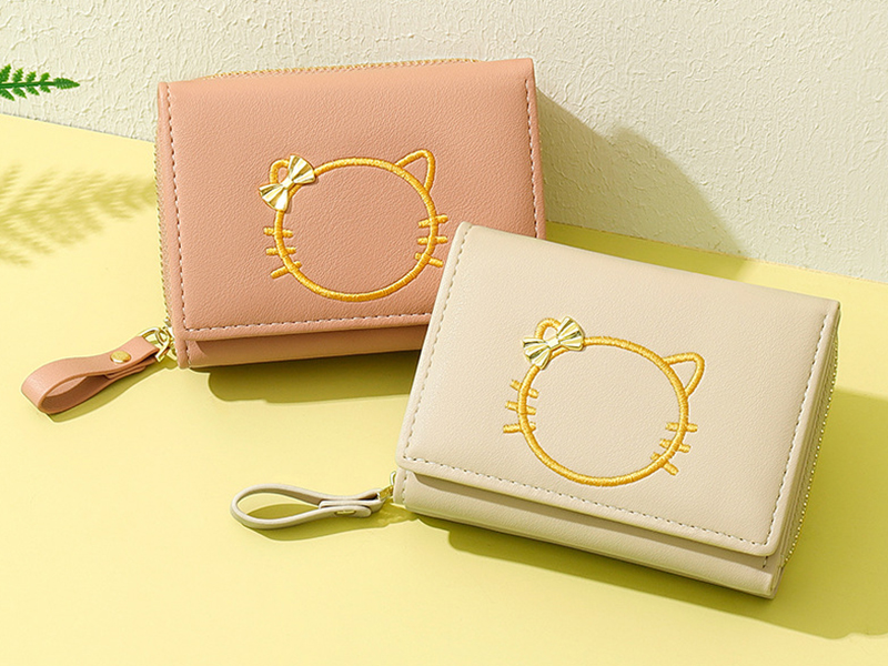 Close-up of two small, foldable women's wallets with cat embroidery and bow details in pink and beige.