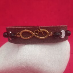 دستبند چرم جیر طبیعی دستساز، تزیین شده با پلاک قلب بینهایت فلزی طلایی، مهره حدید شکل قلب نقره ای و اونیکس مشکی 