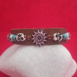 دستبند چرم جیر طبیعی دستساز، تزیین شده با پلاک طرح خورشید، مهره سرامیکی (ژاپنی) گرد گلدار و مهره طرح فیروزه آبی 