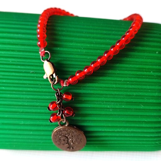دستبند قرمز ترکیبی از مهره ی قرمز گلی شفاف  یک رشته ای  آویز خوشه ای با مهره ی قرمز گلی و سکه برنزی . قفل دارد
