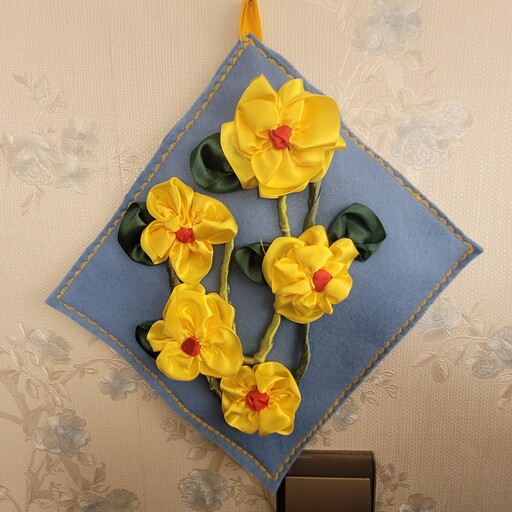 تابلو  روباندوزی  شده با گل های زرد وزمینه کار نمد آبی با دور دوزی با چرخ وبدون قاب ودارای پنج گل وپنج برگ