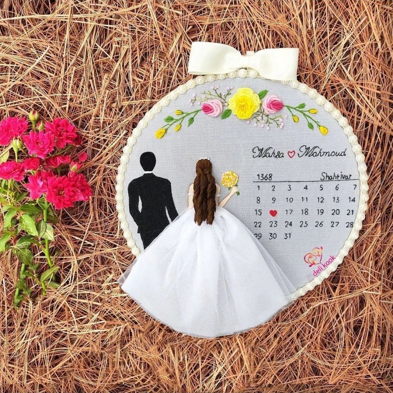 دیوار کوب عروس داماد به همراه تقویم روز ازدواج در کارگاه پلاستیکی تزیین شده با مروارید به سایز 23 سانتیمتر